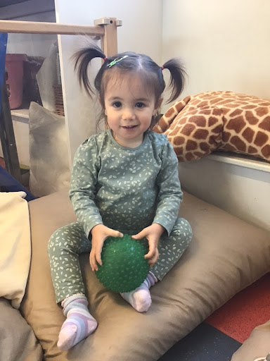 Photo of a young Nursery pupil sitting on a cushion holding a soft green ball in her hands.